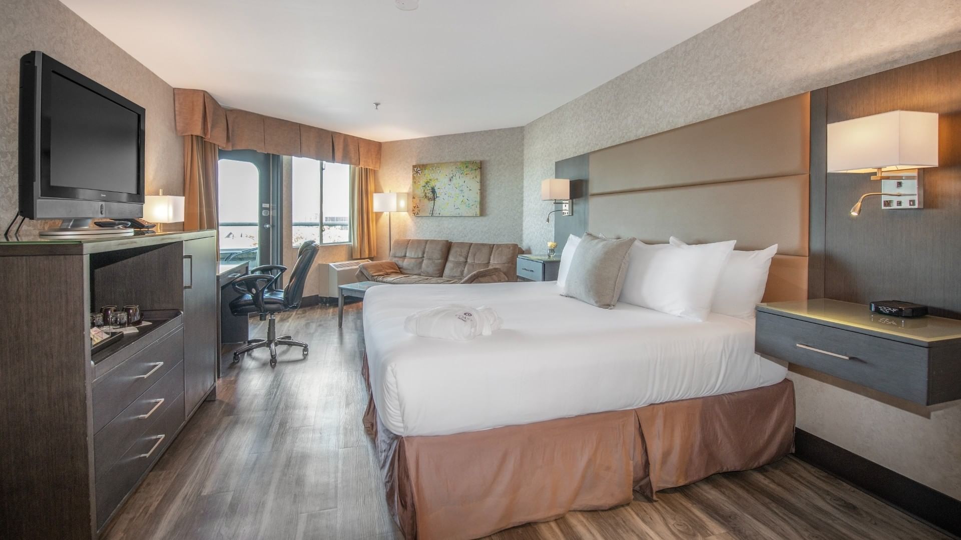 Cozy hotel suite at Coast Lonsdale Quay Hotel featuring a king-size bed, sofa, and a large flat-screen television