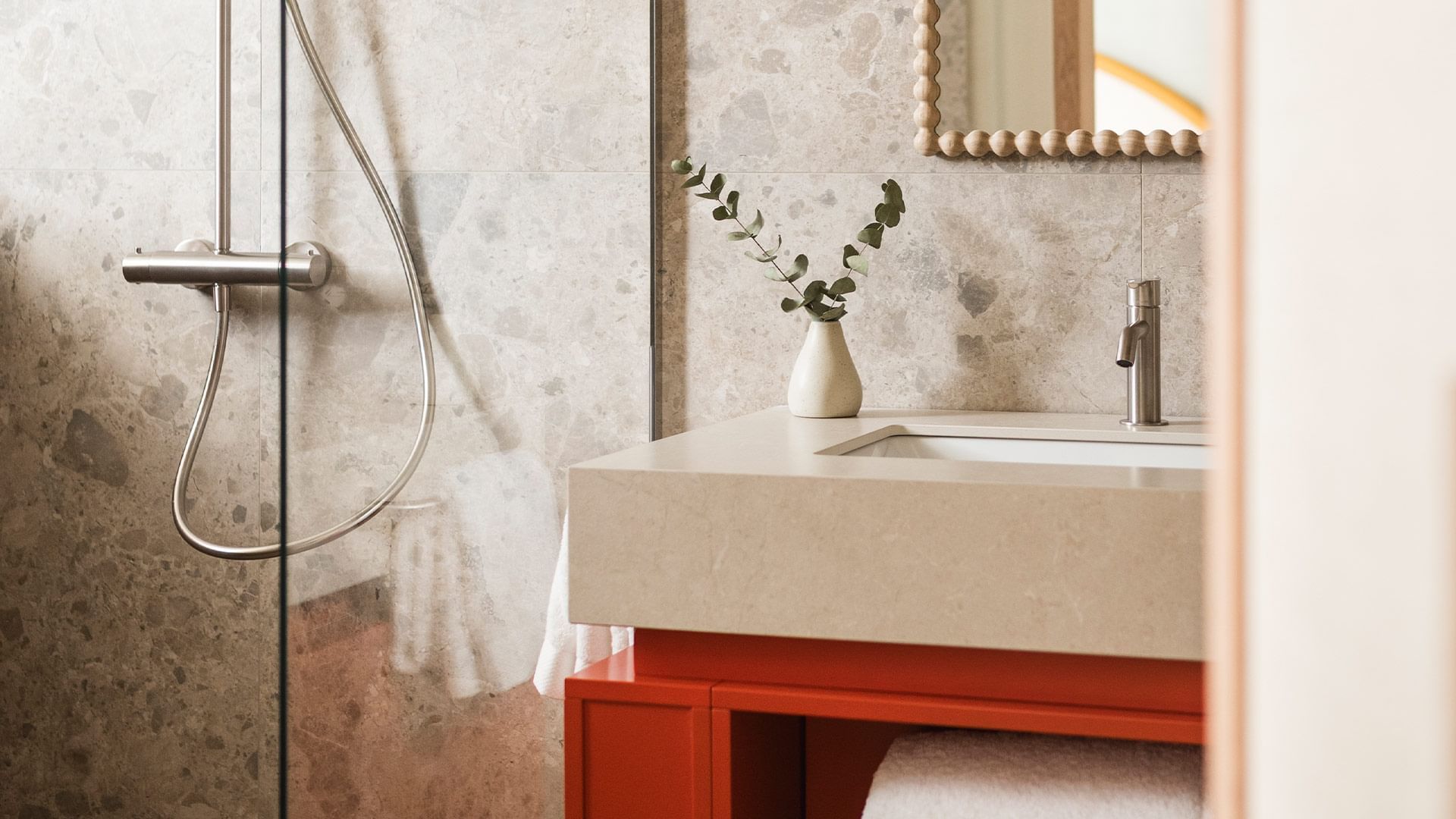 Modern bathroom with a white sink, red cabinet, and a small plant on the counter.