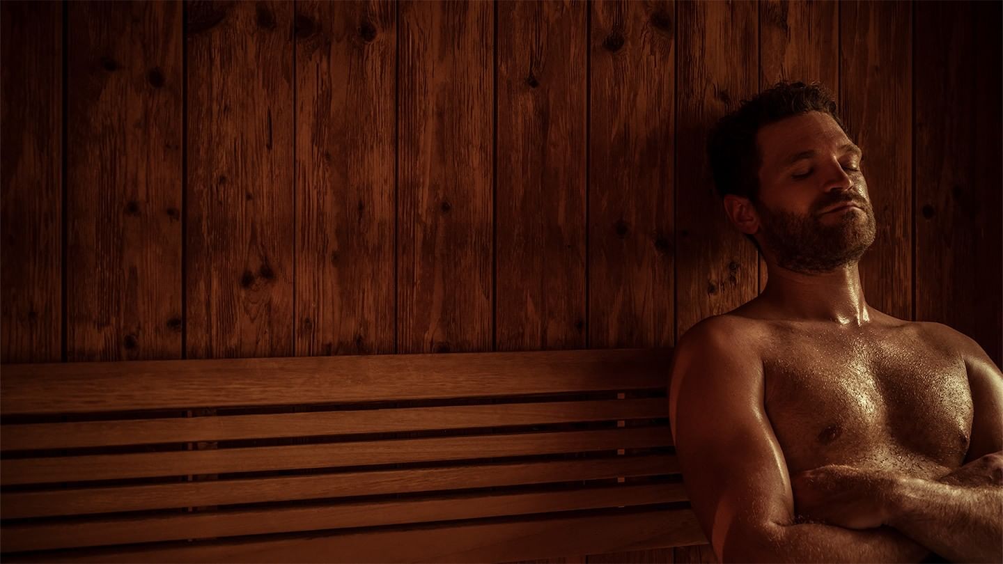 Ein Mann mit geschlossenen Augen entspannt sich auf einer hölzernen Saunabank.