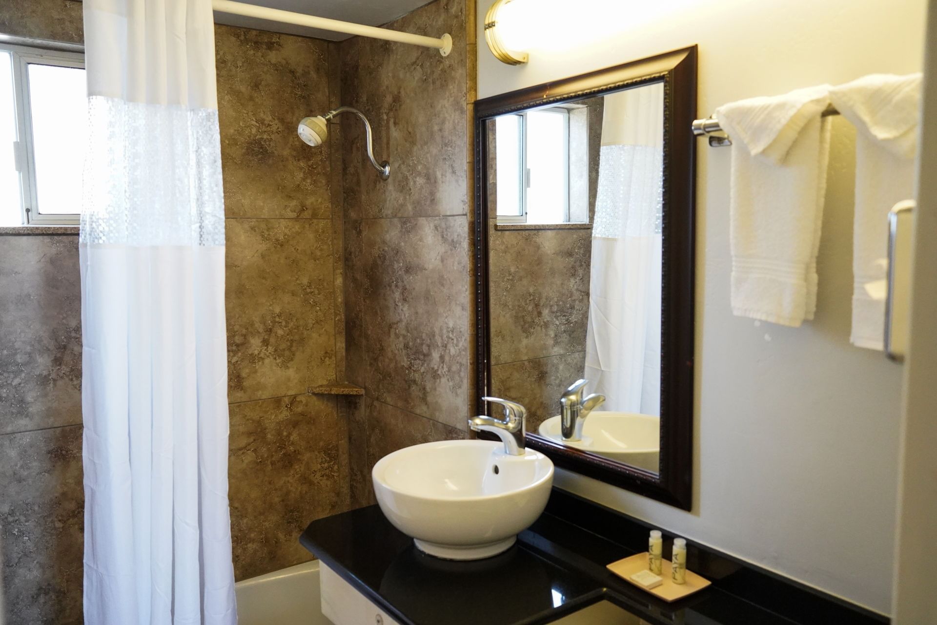 A clean bathroom with a white sink, brown tile, and a shower with a white curtain.