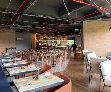 Restaurant interior with dining tables by cushioned chairs under exposed ceiling pipes at Unika Hotels, the restaurant Bogota
