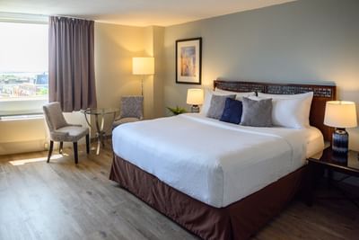 Standard King room seating area by a large window looking out at a sunny town street and the ocean in Rodd Grand Yarmouth