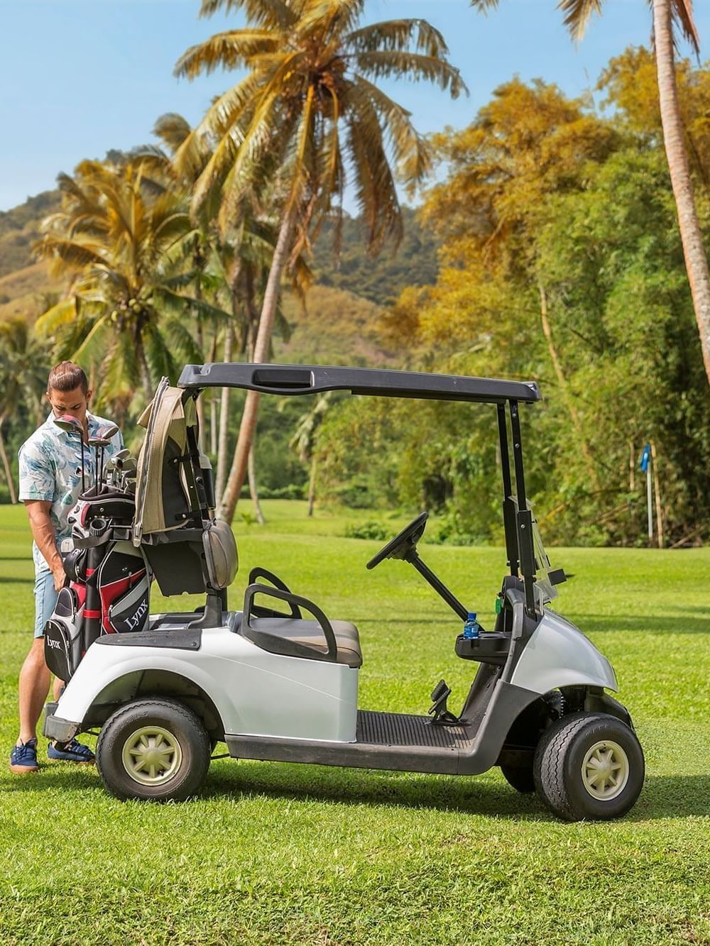 Silver golf cart by a couple with clubs under a canopy of tropical palms at The Naviti Resort - Fiji