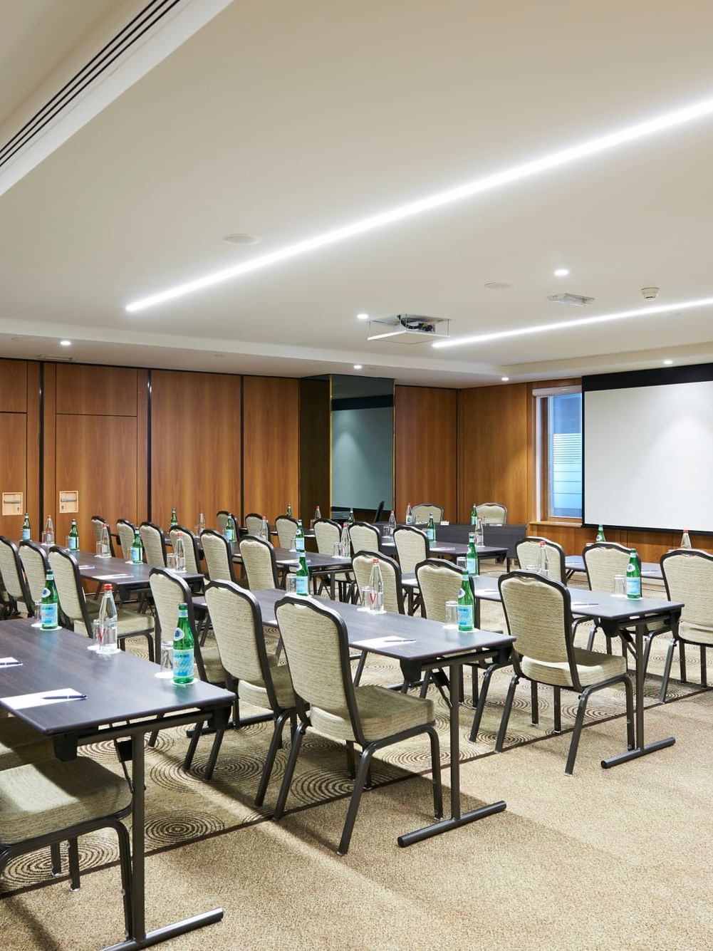 Tables et chaises disposées face à un écran de projection dans la salle Westminster A à Warwick Bruxelles.