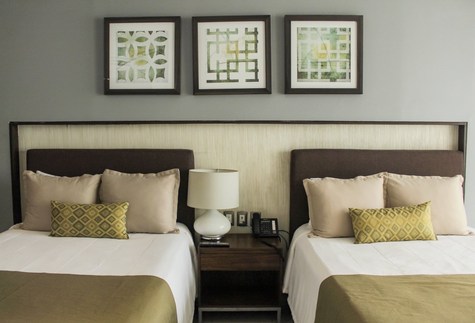 Twin bedroom featuring grey walls, framed wall art, and a bedside lamp with a phone at Sunvivia Mazatlán