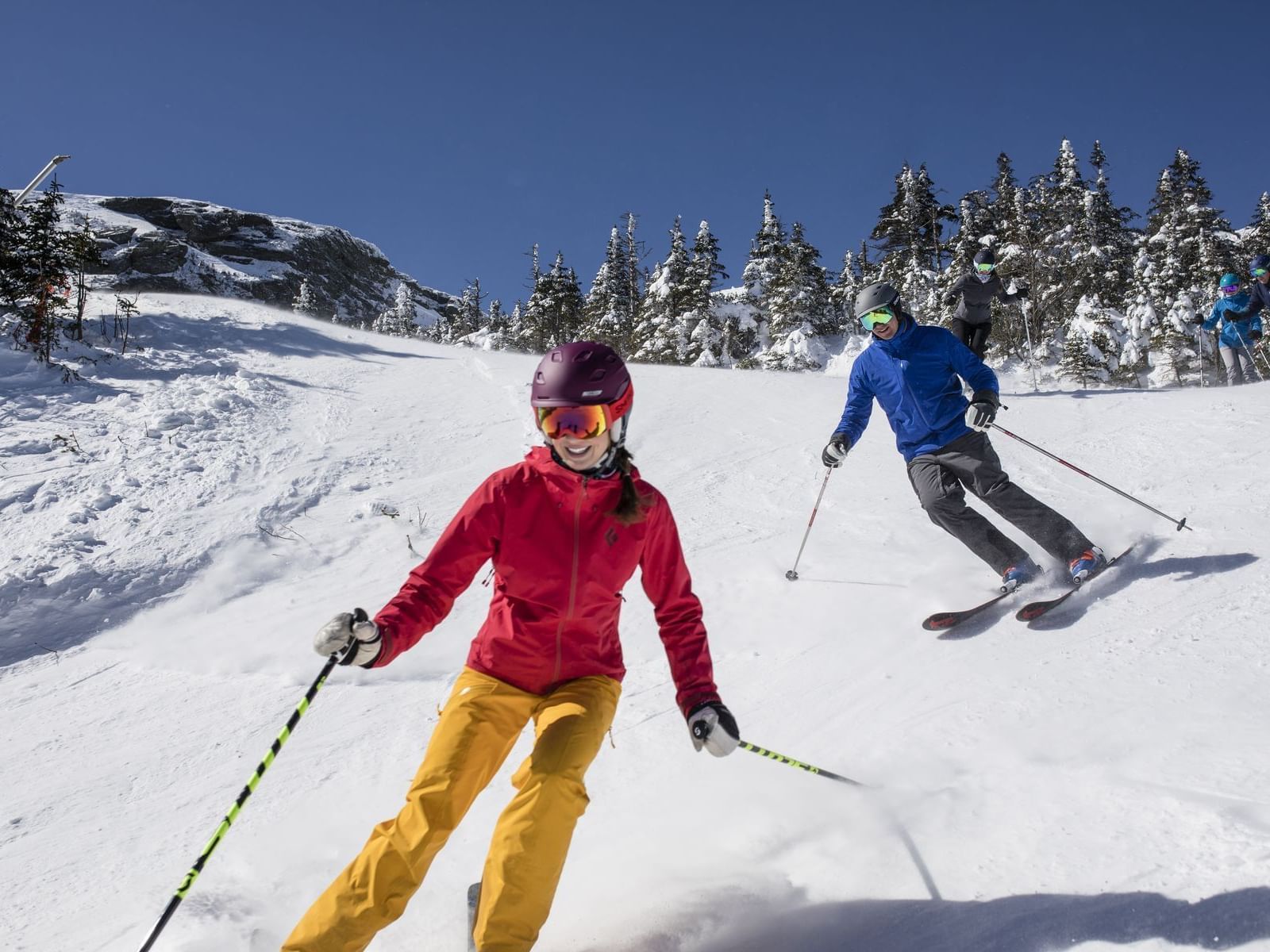 Skiers in motion on a snowy slope with evergreen trees in the background.