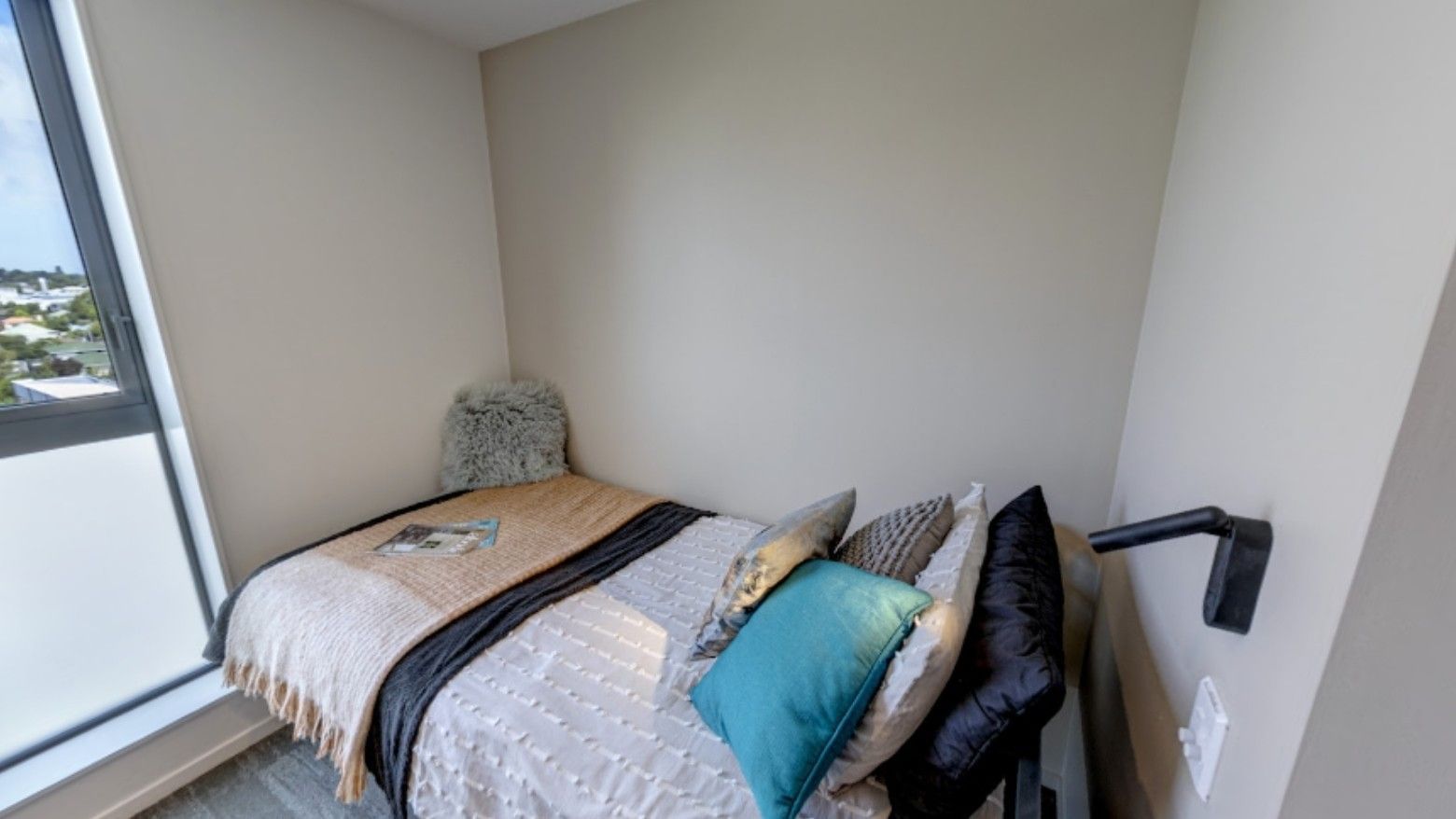 Minimalist bedroom with bed, colorful pillows, throws, and window view in Tupuārangi accommodation.