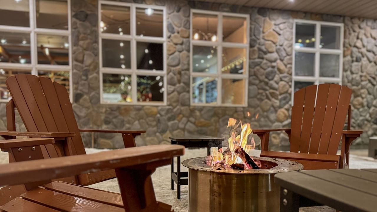 Wooden chairs around a circular fire pit, set against a stone wall.