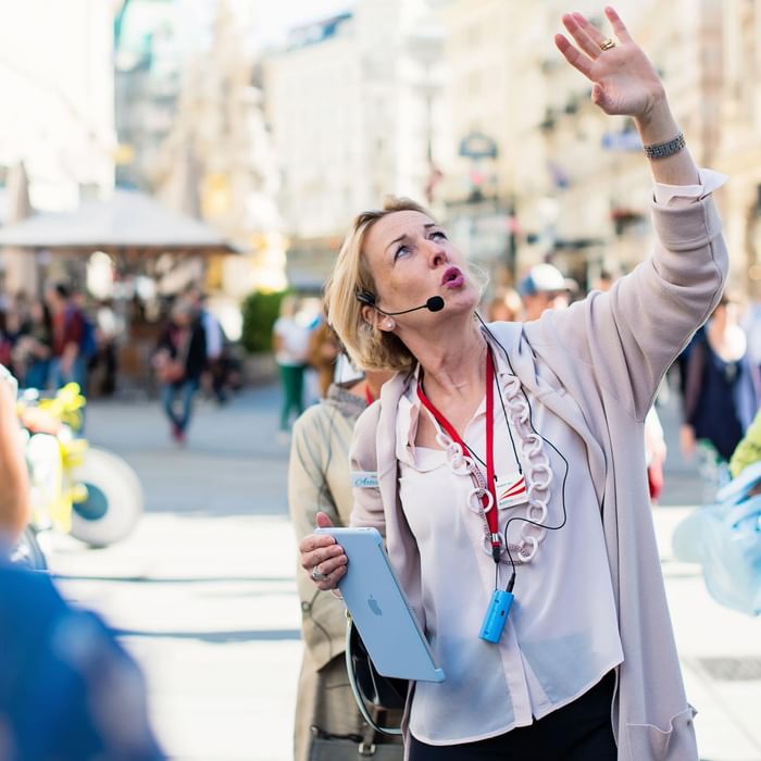 Elisabeth Wolf in a light cardigan raising her hand, holding an iPad, while leading a group tour at Hotel Motto Vienna