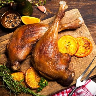 Zwei gebratene Hähnchenschenkel auf einem Schneidebrett mit Orangenscheiben und Kräutern.