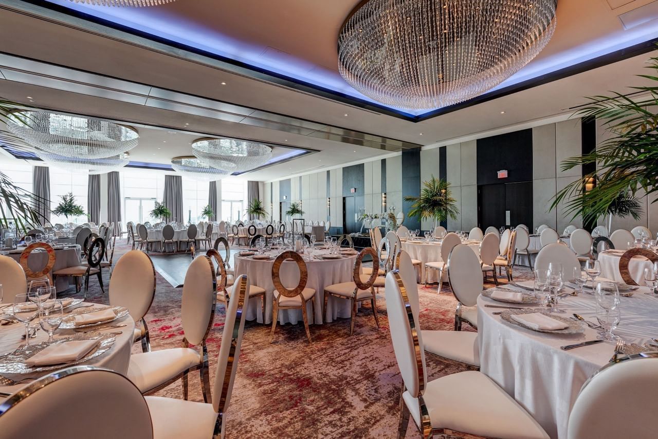 Victory Ballroom at Hotel X Toronto with white round tables and modern chairs and large crystal chandeliers above