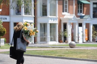 Mujer con flores junto a fachadas blancas bajo cielo despejado cerca de NOI Vitacura