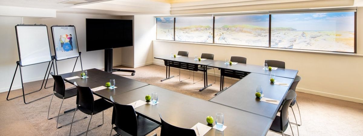 U-shape table set up facing TV by the windows in Waratah at Novotel Sydney International Airport