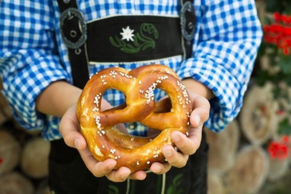 A close-up of a man wearing lederhosen holding soft pretzels for Oktoberfest in Orlando.