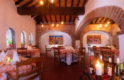 A restaurant interior with tables and chairs, decorative artwork, arched doorways, and lit candles on the tables.