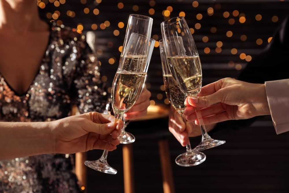 A close up of four people in formalwear toasting with full Champagne flutes. 