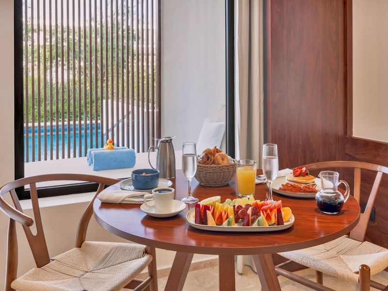 Pancake dish, coffee & a platter of fresh fruit on a coffee table in a room at Live Aqua Resorts and Residence Club