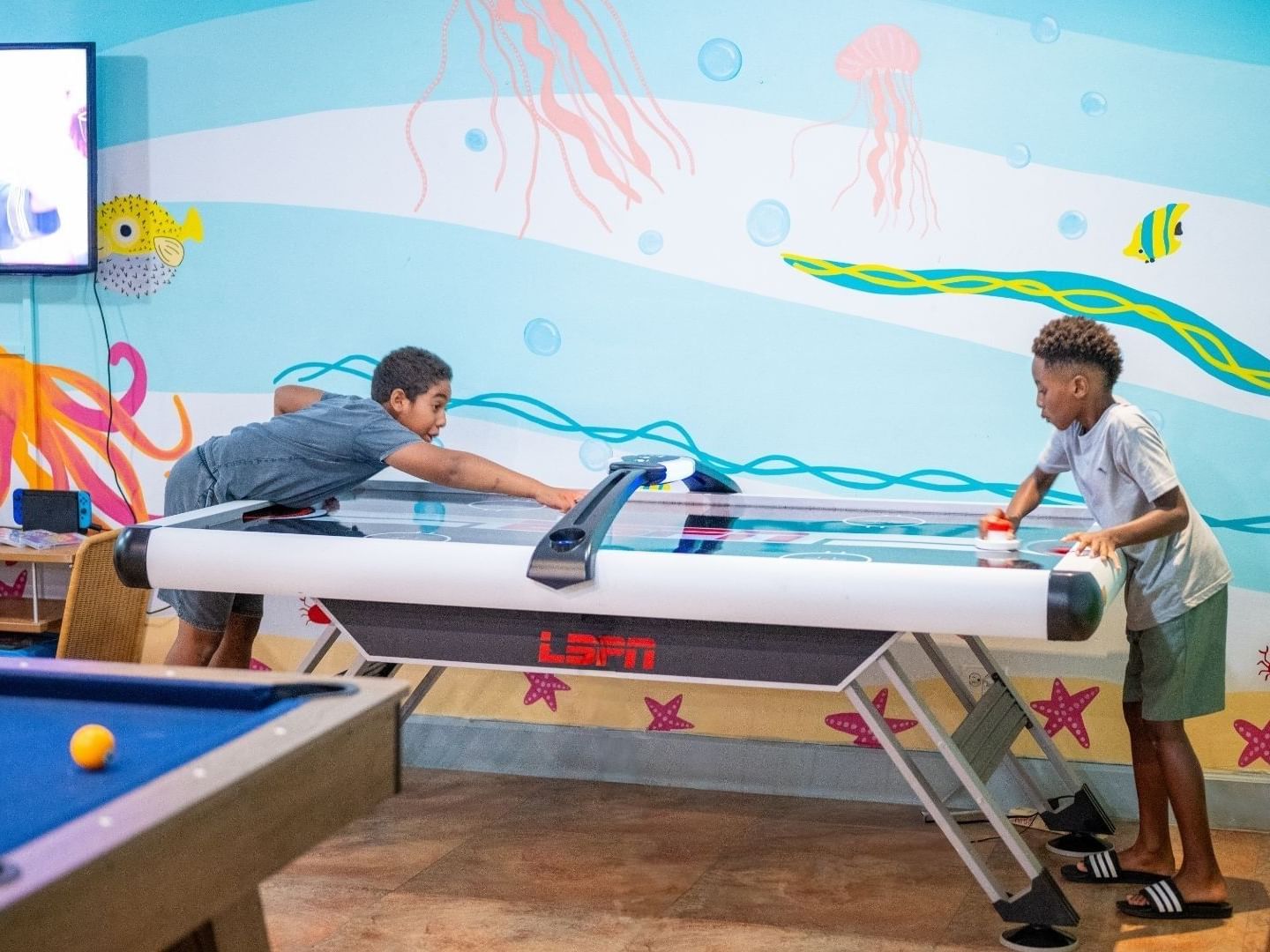 Two kids playing air hockey on a table with an underwater theme at Savannah Beach Hotel.