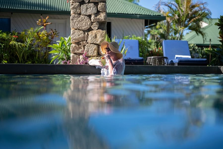 Woman in hat drinking cocktail by the pool at Tokatoka Resort - Fiji International Airport.
