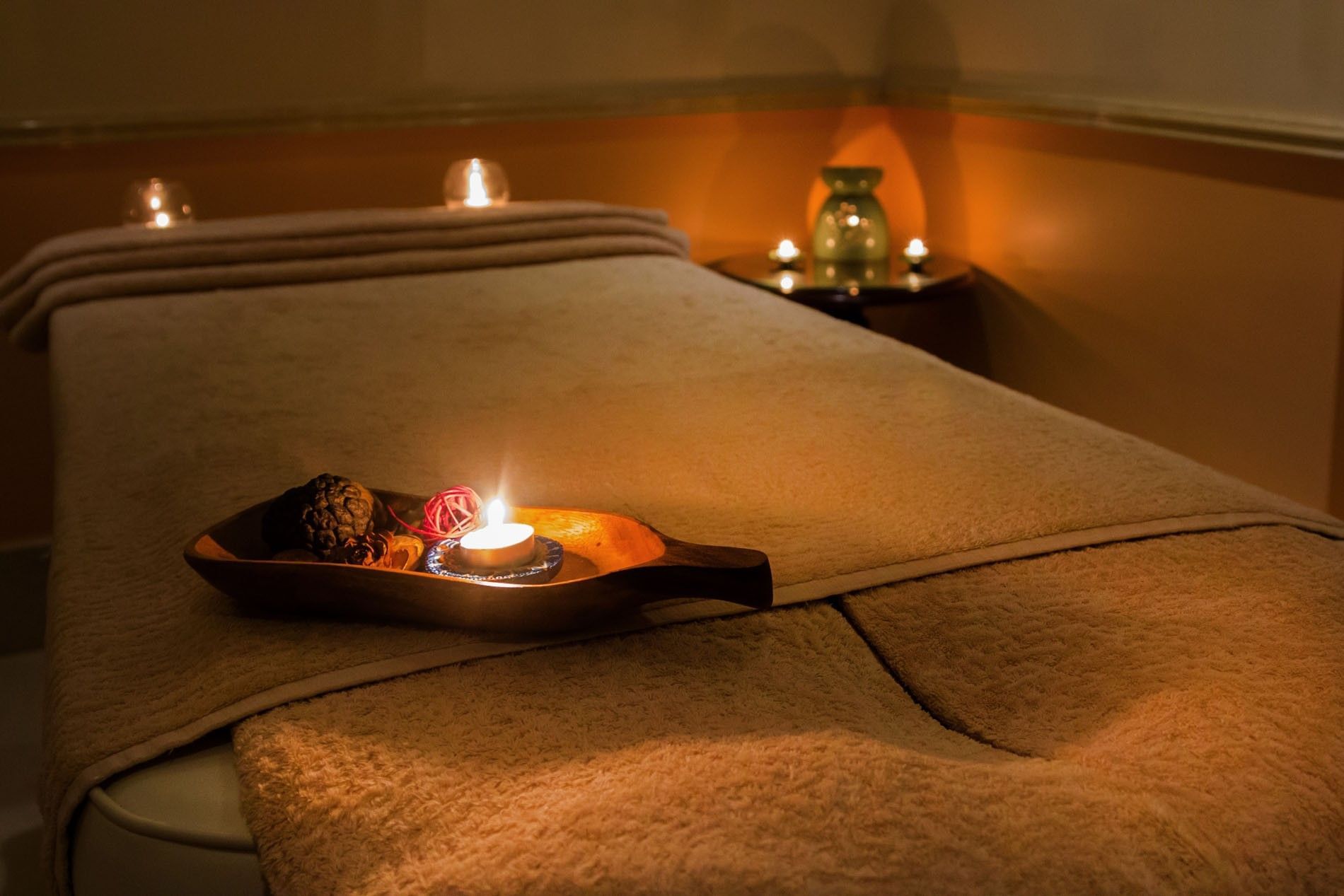 Flickering candles by a wooden tray under soft orange light surrounding a massage table at Warwick Doha Hotel