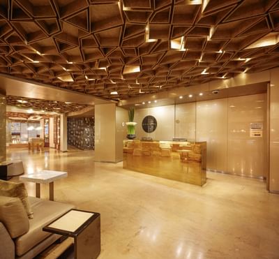 Lobby de hotel con techo de diseño, mostrador de recepción dorado y mobiliario elegante.