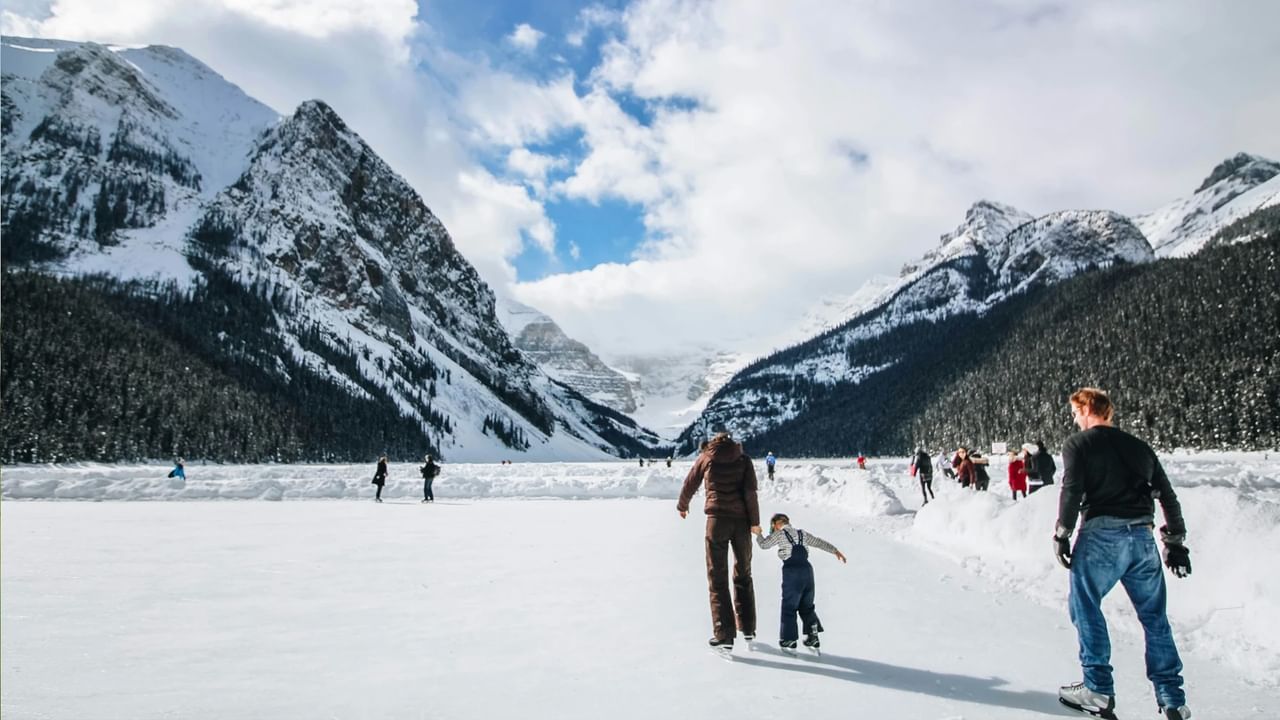 Families skate on a frozen Lake Louise on a sunny day.