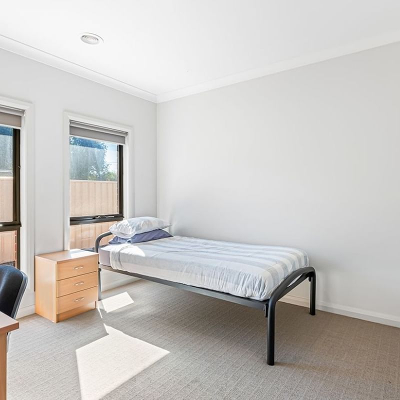 A clean single room with a bed, desk, and window at La Trobe University Regional Housing – Mildura.