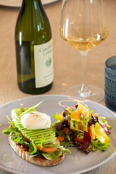 Plate with salad and avocado toast, wine glass, and wine bottle at Ellipse Grace Bay