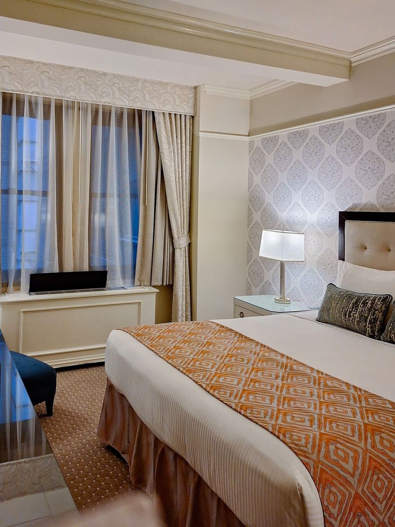 Close-up of a hotel bed with an orange geometric runner and bedside table lamp in Premier Suite at Warwick New York 
