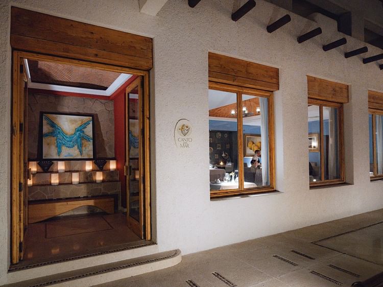 The inviting entrance to Canto del Mar restaurant at Marquis Los Cabos Resort with a vibrant art piece and candlelight