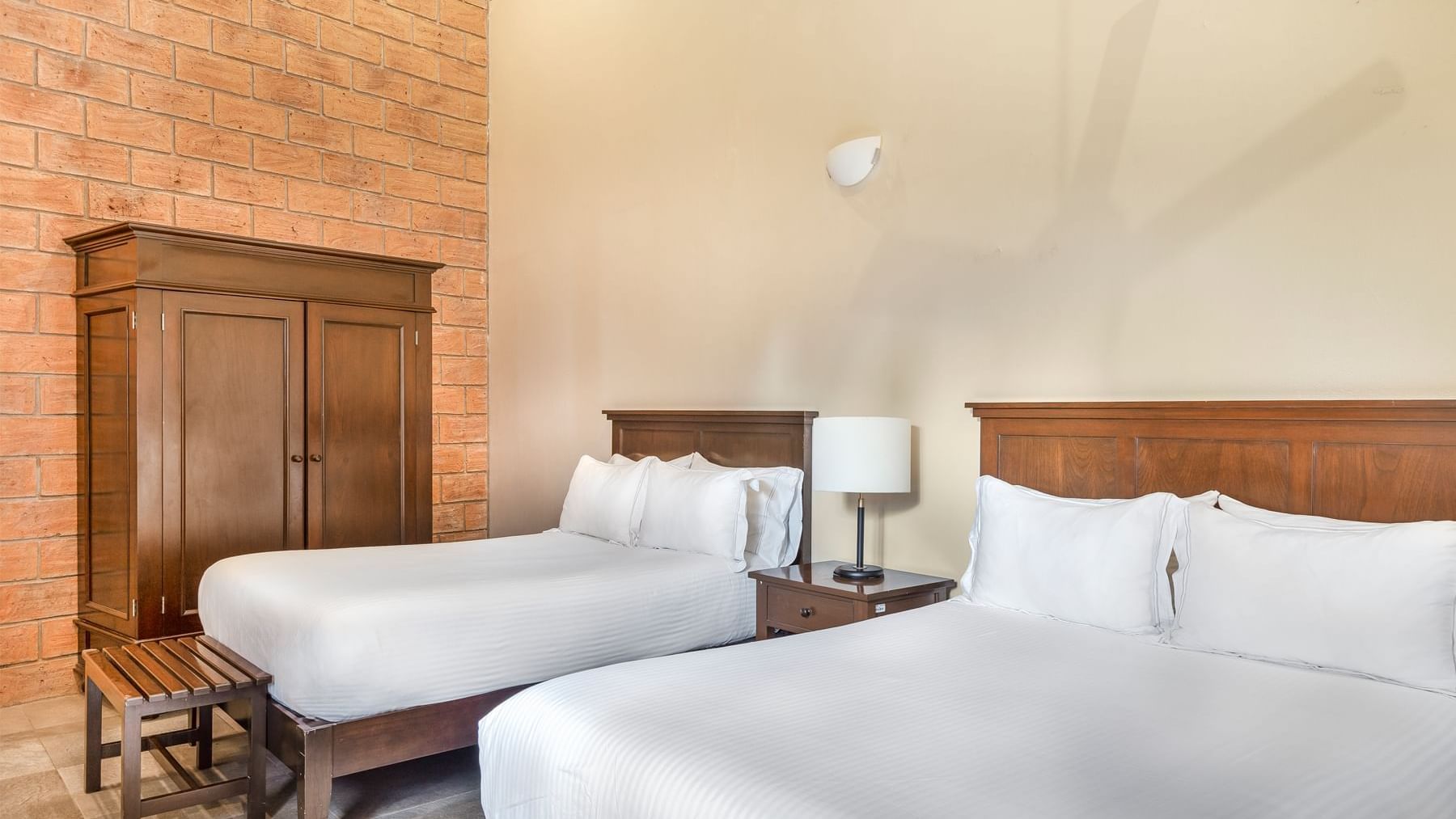 Two queen-sized beds and a rustic brick wall in a room at the Curamoria Collection