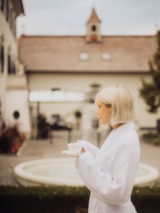 A lady in a bathrobe having a coffee outside at Imlauer Hotel