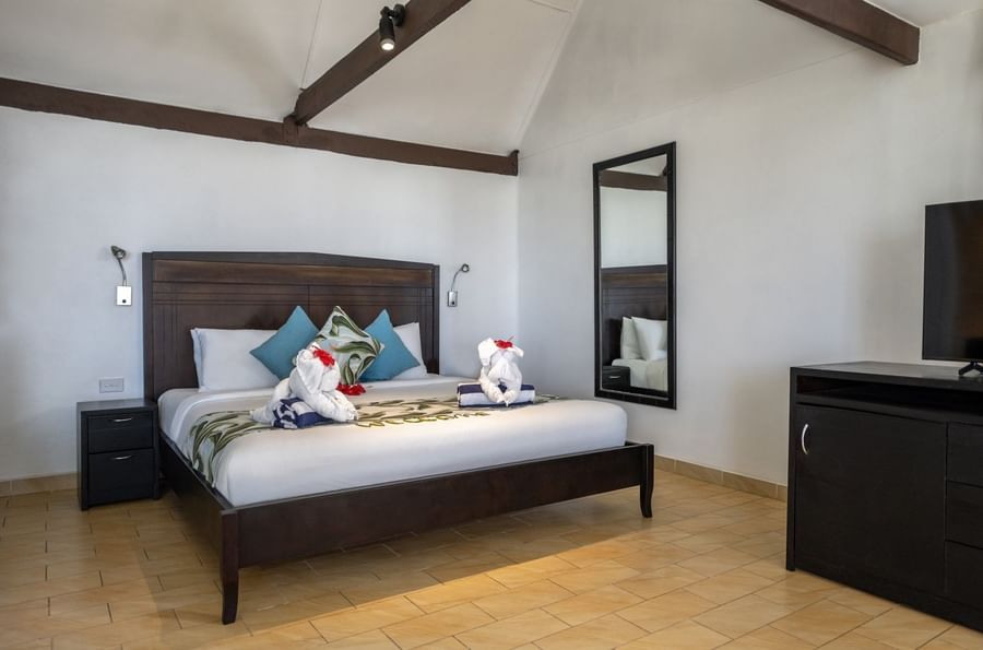 Dark wood bed & elephant towel art by a tall mirror in Beach Front Bure with Plunge Pool at Tambua Sands Beach Resort