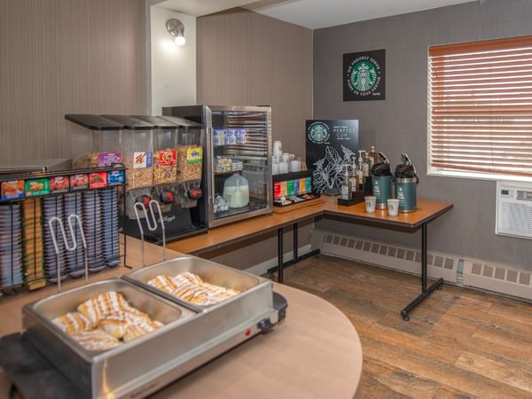 A room with a breakfast setup, featuring pastries, cereal and coffee.