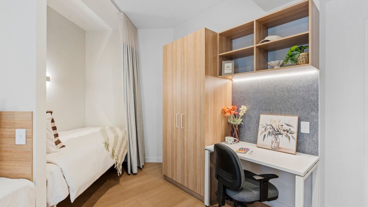 Modern room at UniLodge Brisbane City with bed, desk, and wooden closet.