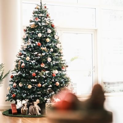 Dekorierter Weihnachtsbaum vor Glastür mit Geschenken am Boden, umgeben von hellem Licht.