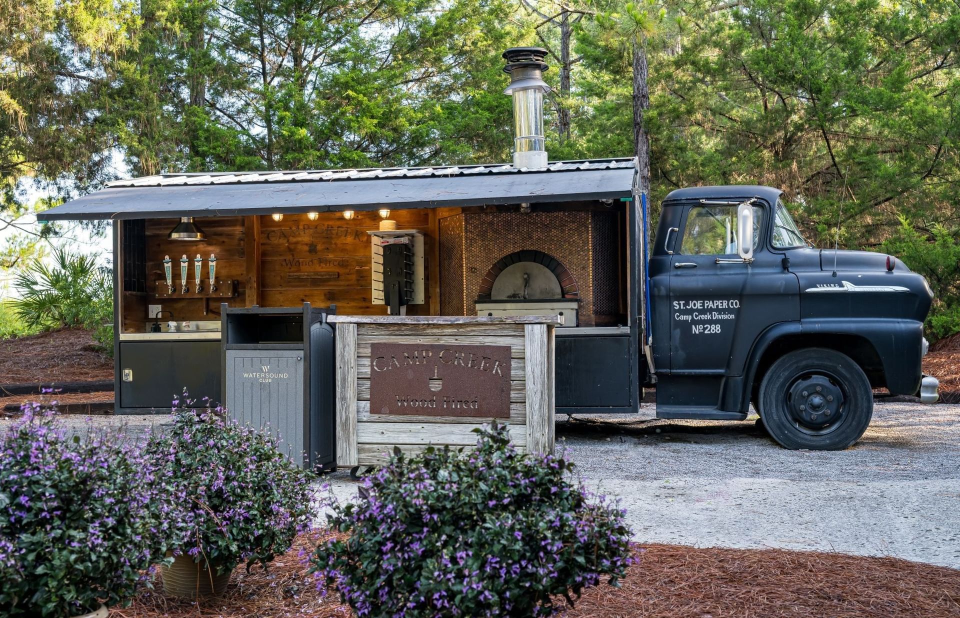 Vintage black truck converted into a wood-fired pizza station surrounded by purple flowers at Camp Creek Inn