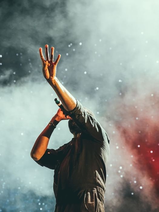 Performer holding a microphone by a raised hand under smoky stage lights and sparkles near Warwick Melrose Dallas