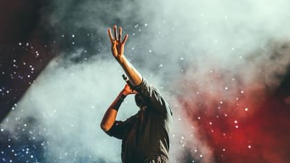 Performer holding a microphone by a raised hand under smoky stage lights and sparkles near Warwick Melrose Dallas