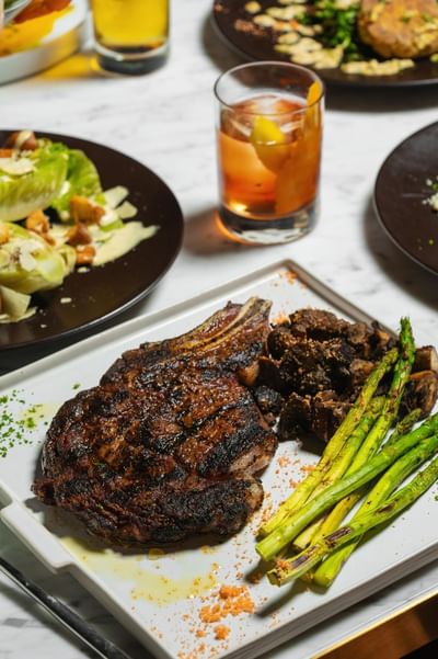 Beautifully grilled ribeye steak with asparagus and mushrooms served with a cocktail & various dishes at Cypress & Oak