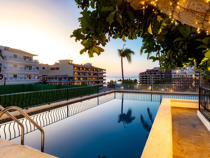 Calm rooftop swimming pool reflecting tall palm trees against a glowing orange sunset sky at Casa Dona Susana