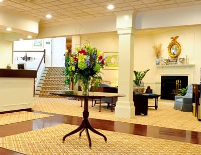 Lobby area with a flower vase on a table near the fireplace and carpeted stairs at Farmington Inn and Suites