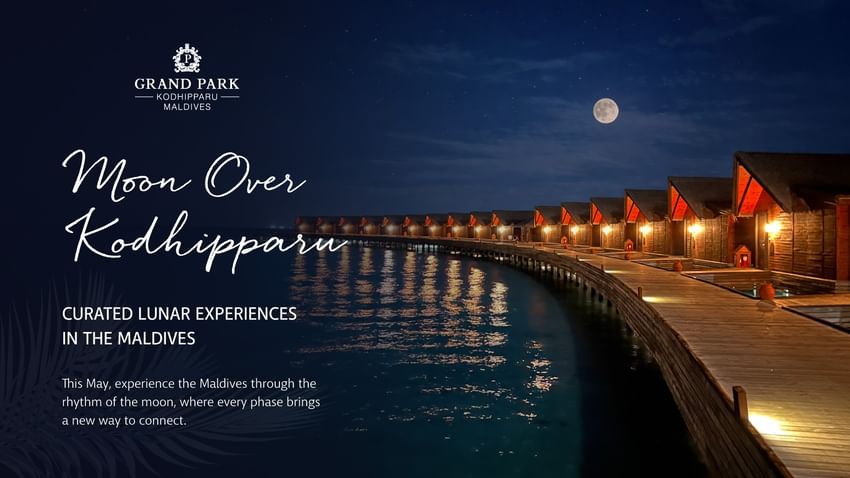 Illuminated waterfront bungalows under a full moon at Grand Park Kodhipparu.