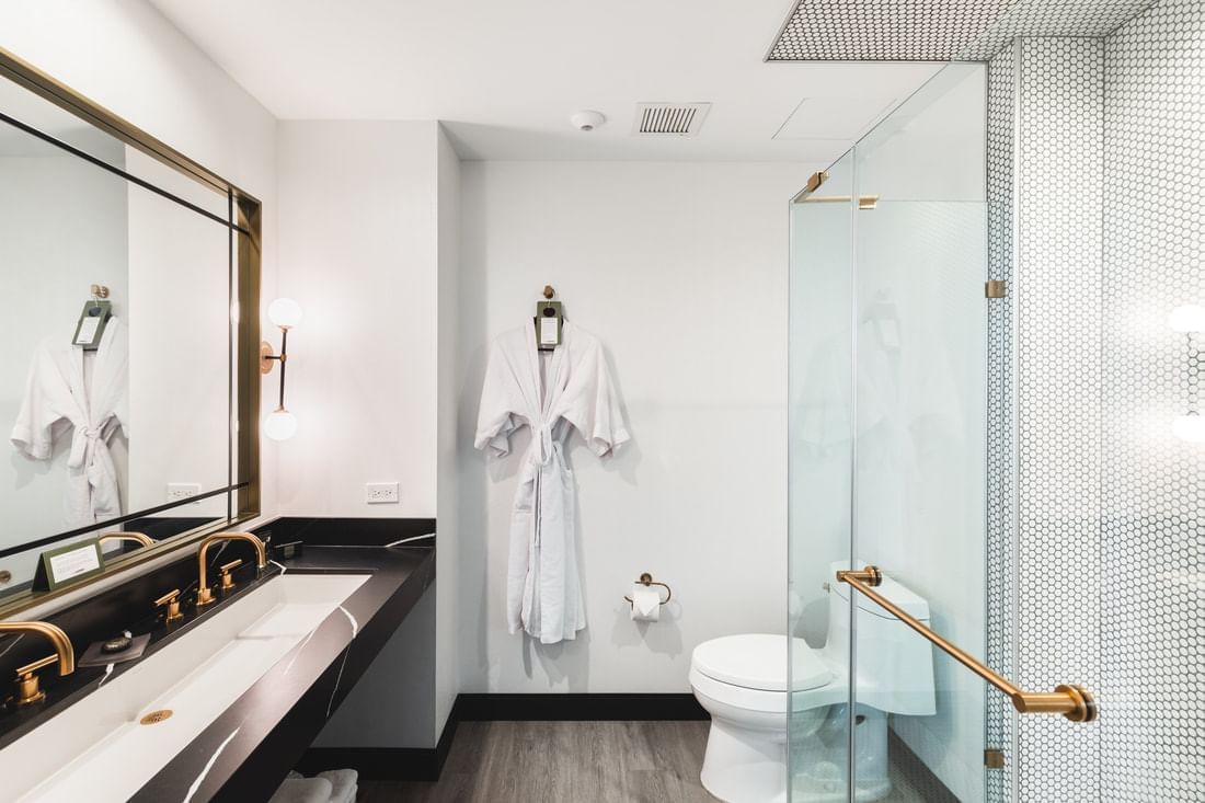 A modern hotel bathroom with a large mirror, double vanity, toilet, and glass-enclosed shower.