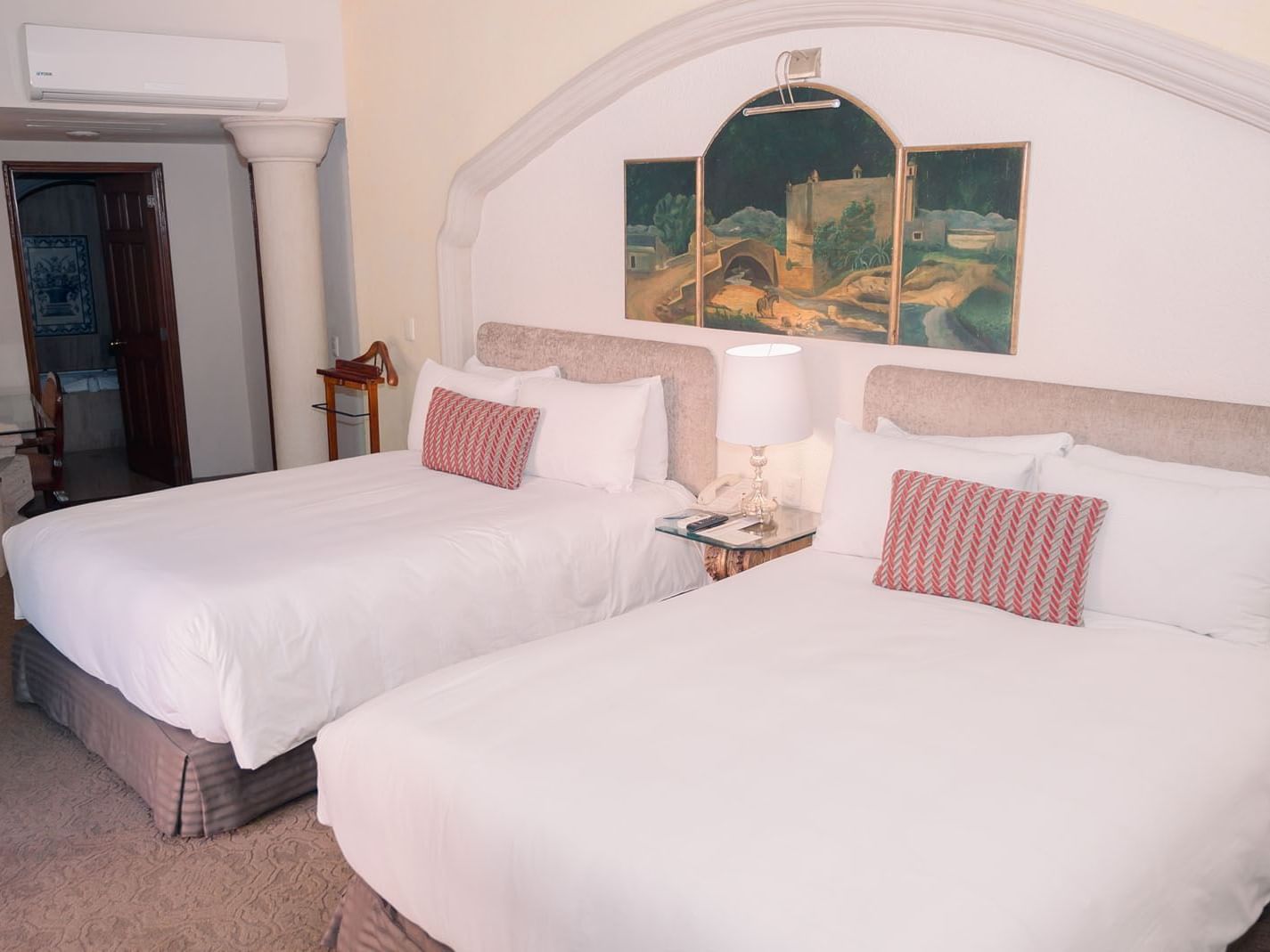 Dos camas con sábanas blancas y almohadas rojas y blancas en una habitación con pinturas.