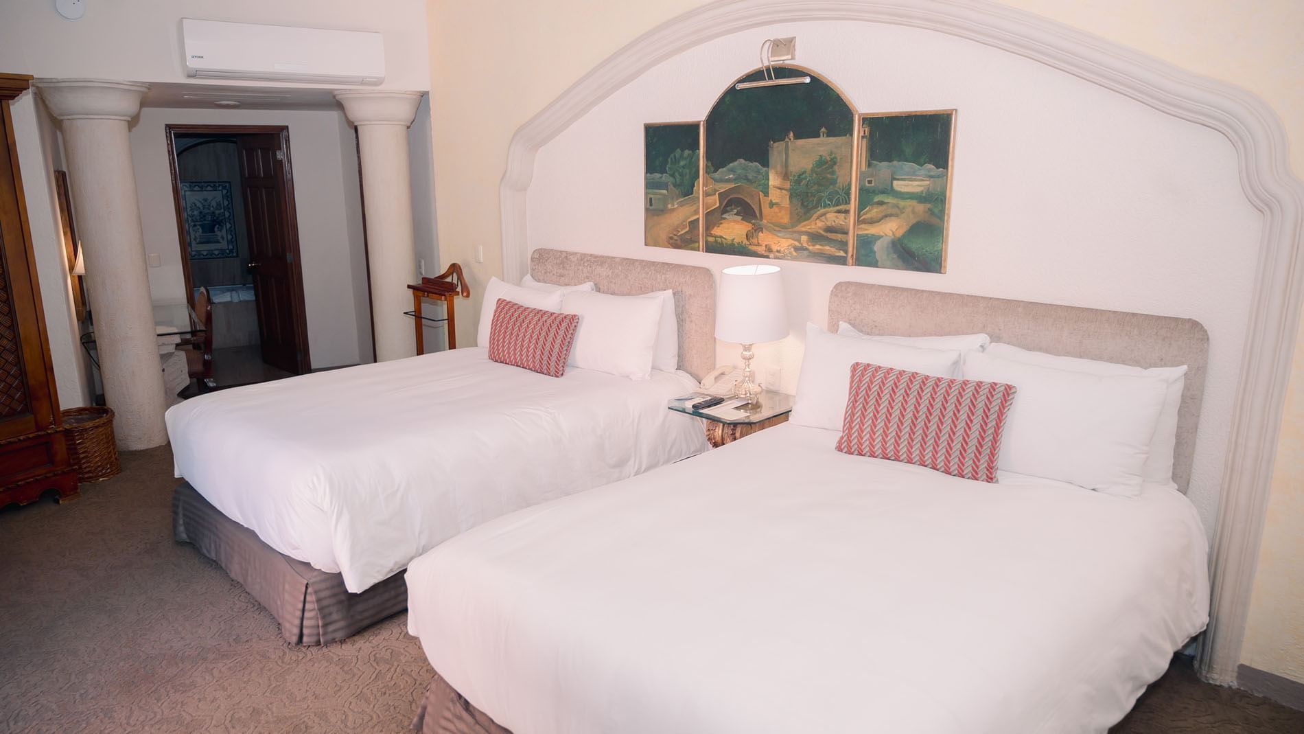 Dos camas con sábanas blancas y almohadas rojas y blancas en una habitación con pinturas.