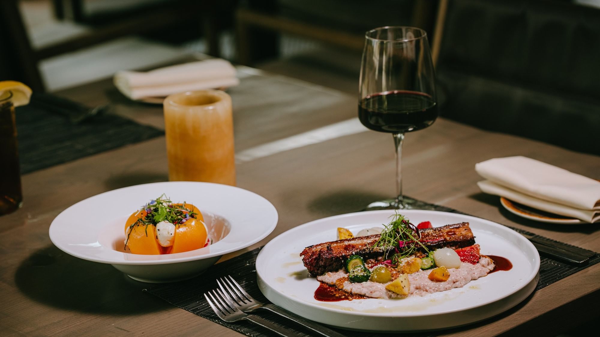 A dining table set with two dishes, a wine glass, and a candle, ready for a meal.