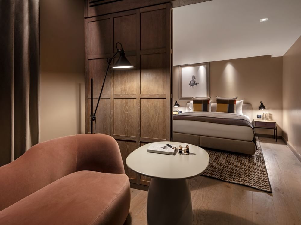 Cozy lounge area and a bed separated by a wooden partition in the Junior Suite at The Londoner Hotel