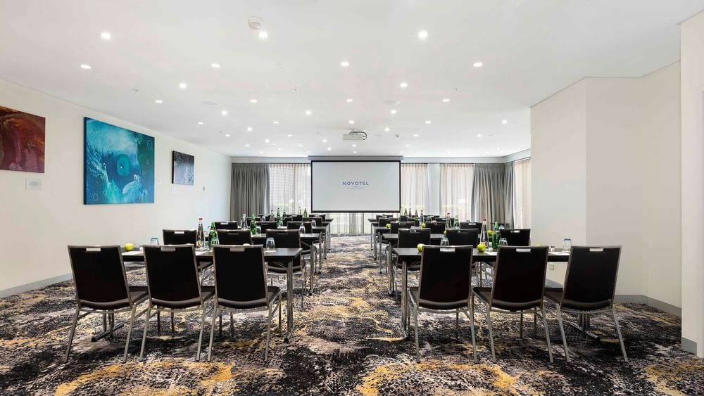 Theater-style table set-up facing the projector screen in The Barossa Room at Novotel Sydney on Darling Harbour