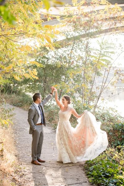 Radiant bride twirls in her gown, dancing with her groom on a path at Lake Natoma Inn